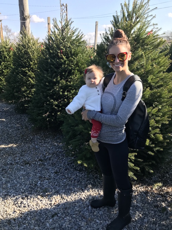 A parent holding their baby in a pre-cut Christmas tree lot.